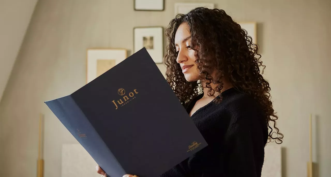 Femme brune et frisée qui tient dans ses mains une brochure Junot