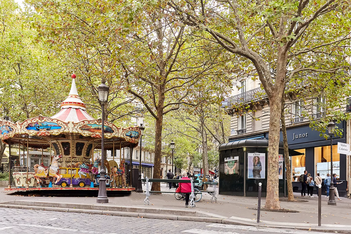 Place Lino Ventura dans le 9ᵉ arrondissement de Paris, avec son carrousel coloré et l’agence Junot Martyrs en arrière-plan.