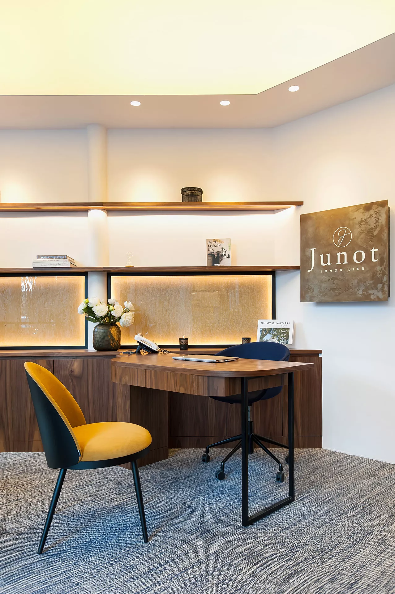 Intérieur d'une agence Junot, vue sur un bureau en bois brun et une chaise orangée