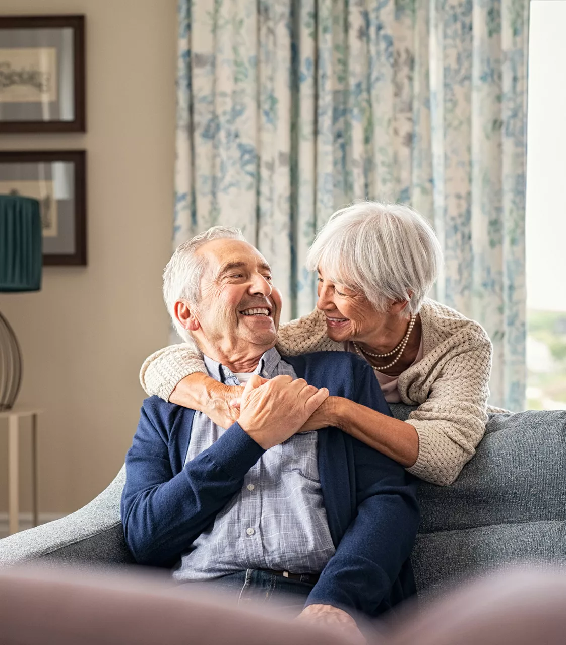 Senior couple hugging on a sofa, having entrusted the sale of their property in return for a life annuity to Junot